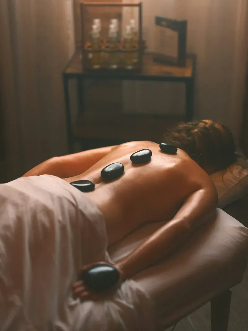Mulher deitada com pedras quentes nas costas durante massagem em Curitiba.